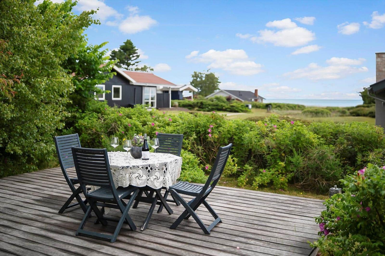Wooden terrace with table and chairs, view of house and sea.