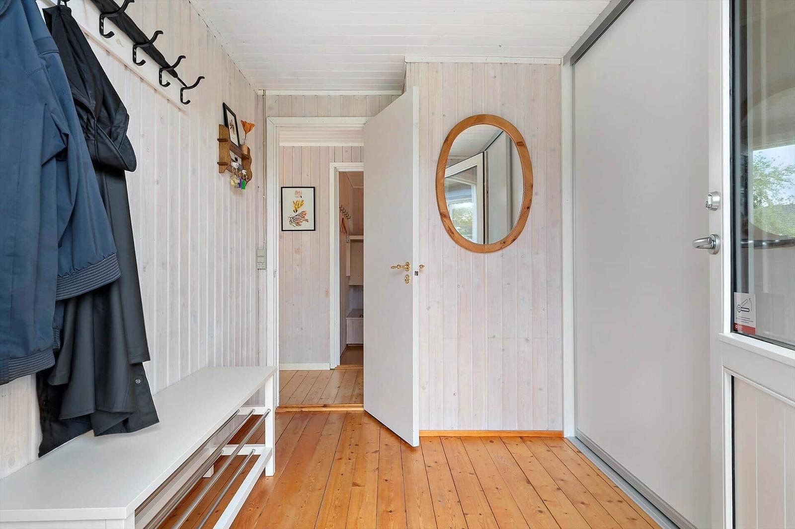 Hallway with wooden floor, coat rack, and round mirror on the wall.
