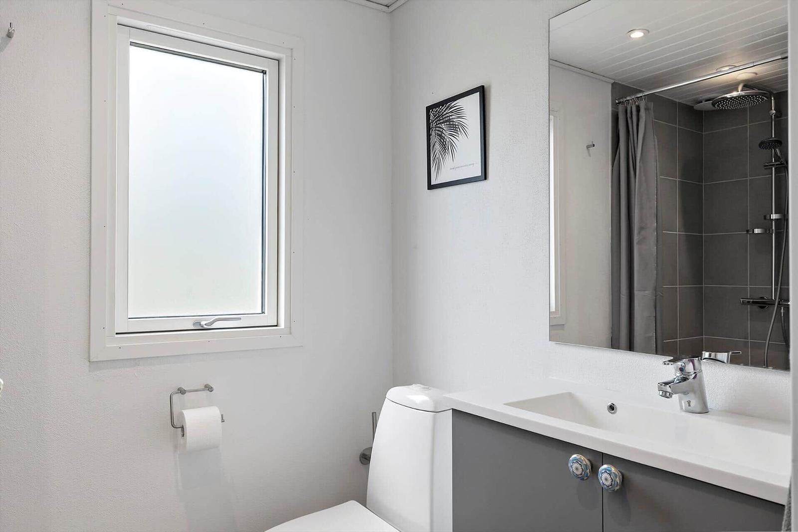 Bathroom with toilet, sink, and shower. Window and mirror are present.