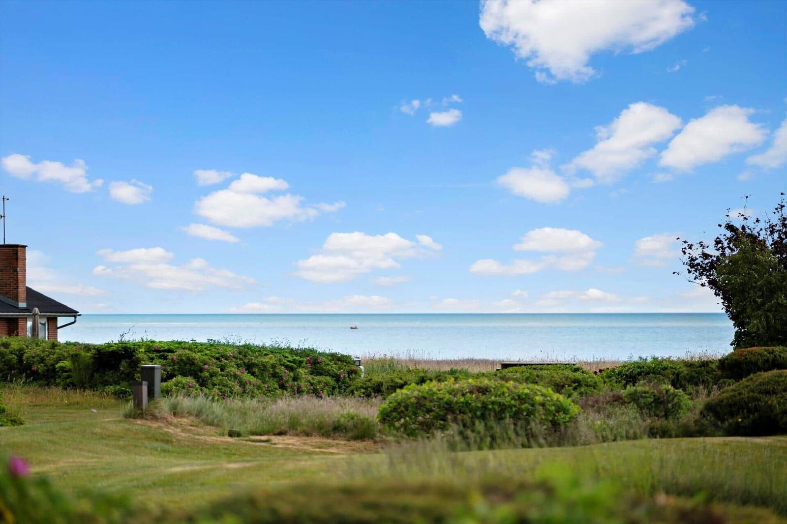 House with sea view and green meadows under blue sky with white clouds.
