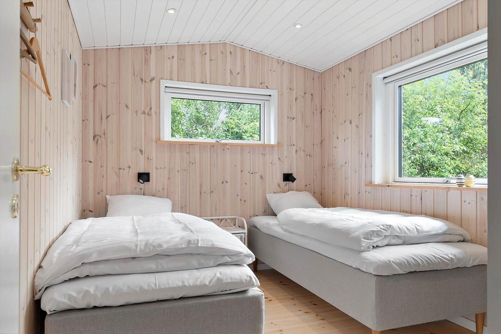 Two beds in a wooden room with windows and white bedding.
