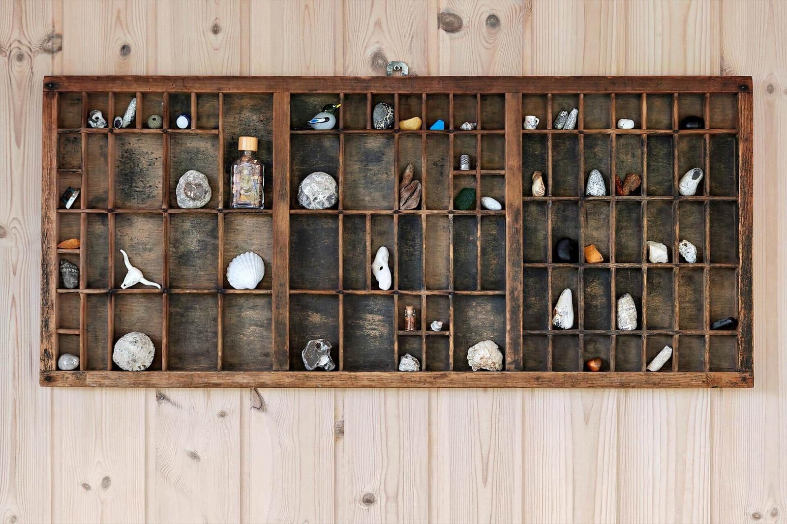 Wooden rack with compartments filled with stones, skulls, and small objects on a wooden wall.