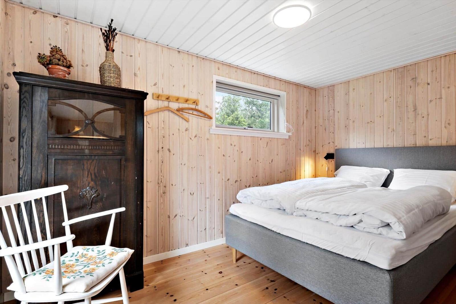 Bedroom with wooden walls, bed, wardrobe, and chair.