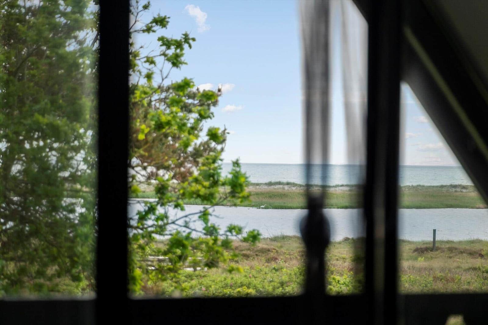 Durch ein Fenster blickt man auf einen See und das Meer.