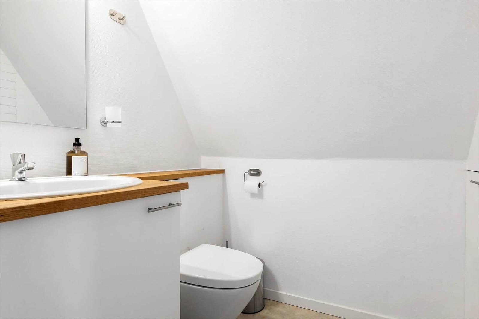 Badezimmer mit Waschbecken, Toilette und Spiegel an schräger Decke.