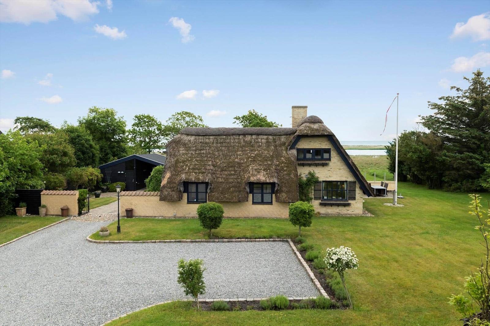 Haus mit Strohdach, Garten und Blick aufs Wasser.