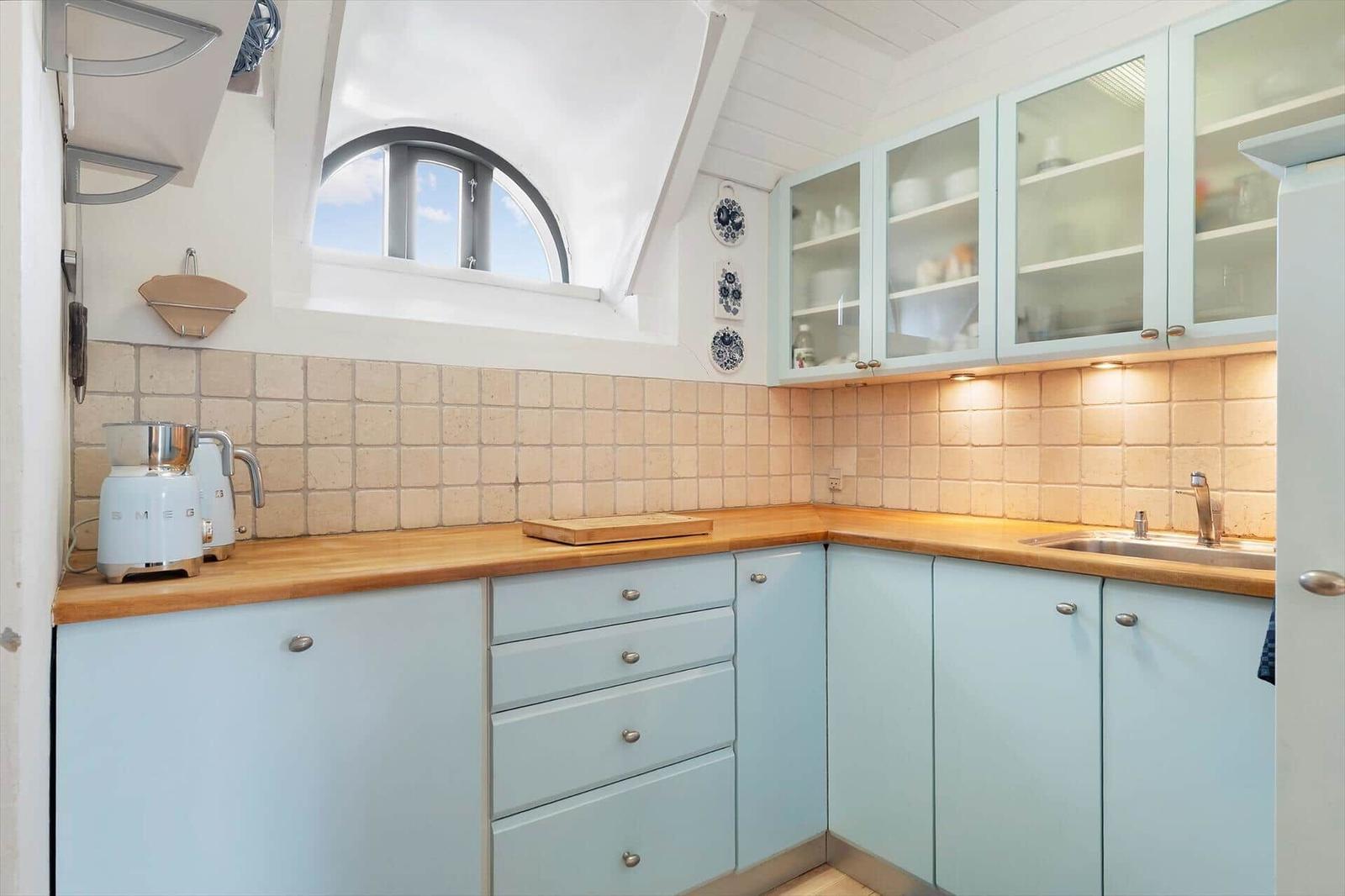 Küche mit hellblauen Schränken, Holzoberfläche und Badezimmerfenster.