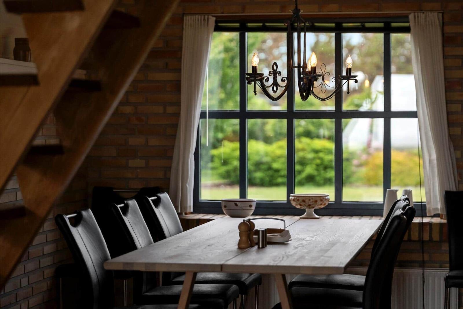 Esszimmer mit Holztisch, schwarzen Stühlen und großem Fenster mit Blick auf Garten