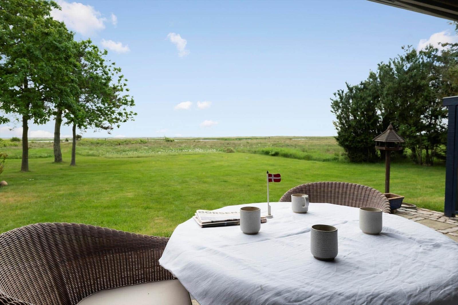Rundtisch mit Tassen und dänischer Flagge auf Terrasse mit Blick auf Grasland und Bäume.