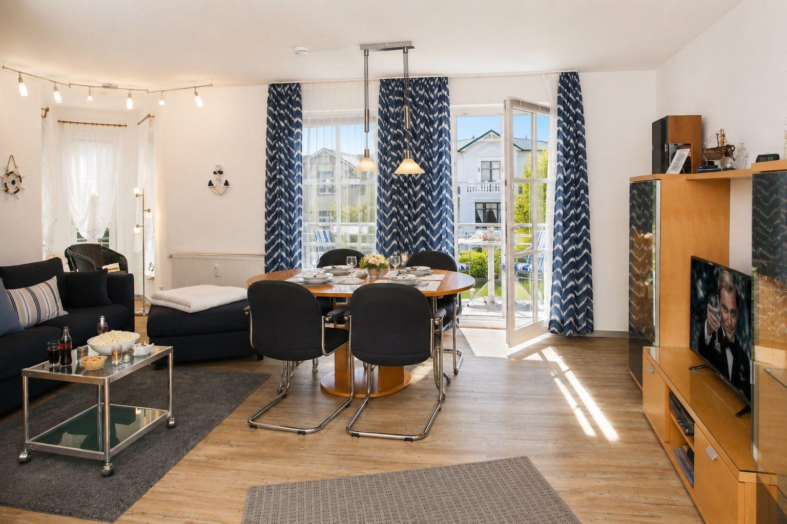 Wohn- und Essbereich mit Balkon, Tisch, Stühlen, Sofa und Fernseher.