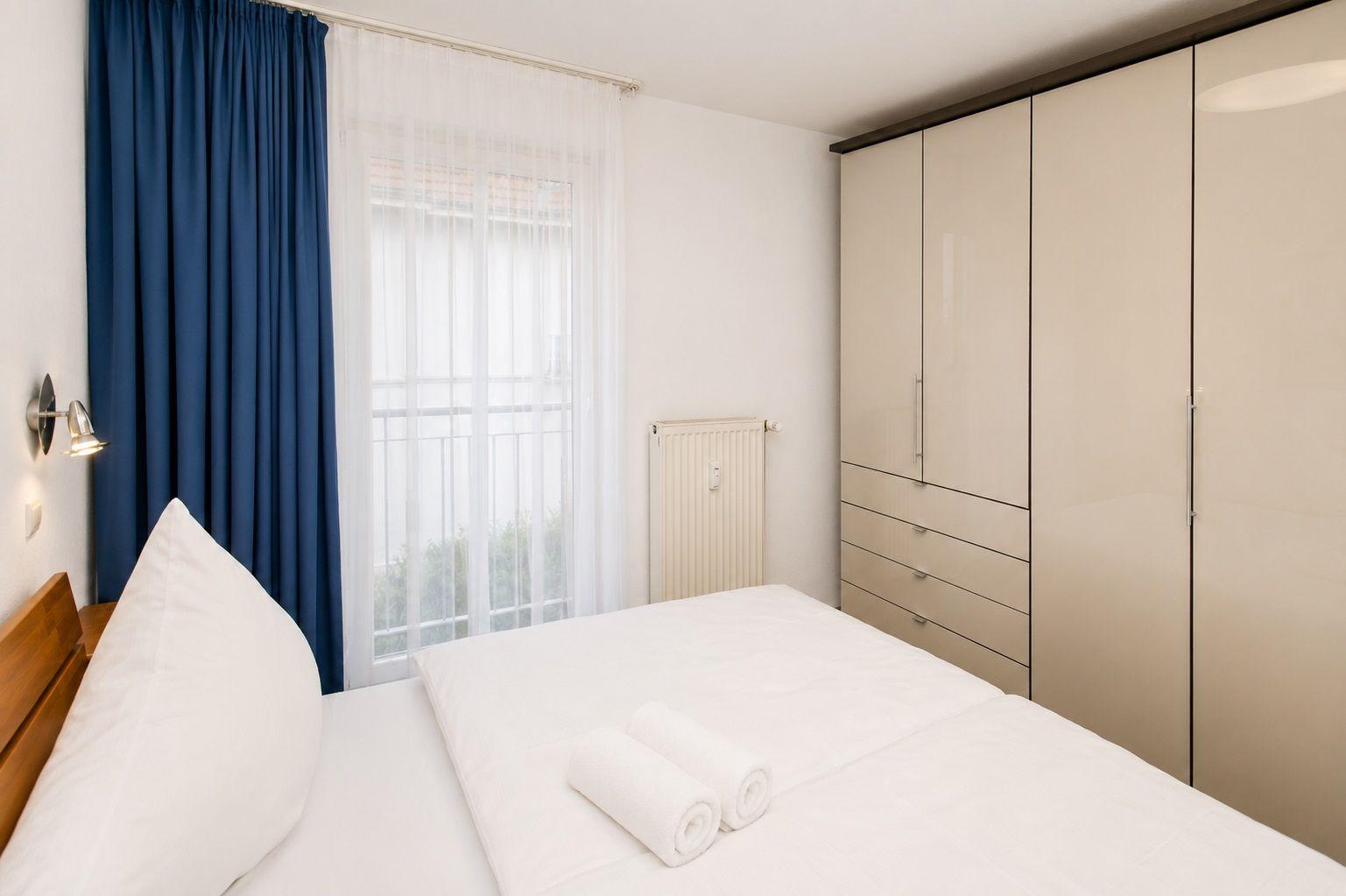 Schlafzimmer mit Bett, Kleiderschrank und Fenster mit Vorhängen.