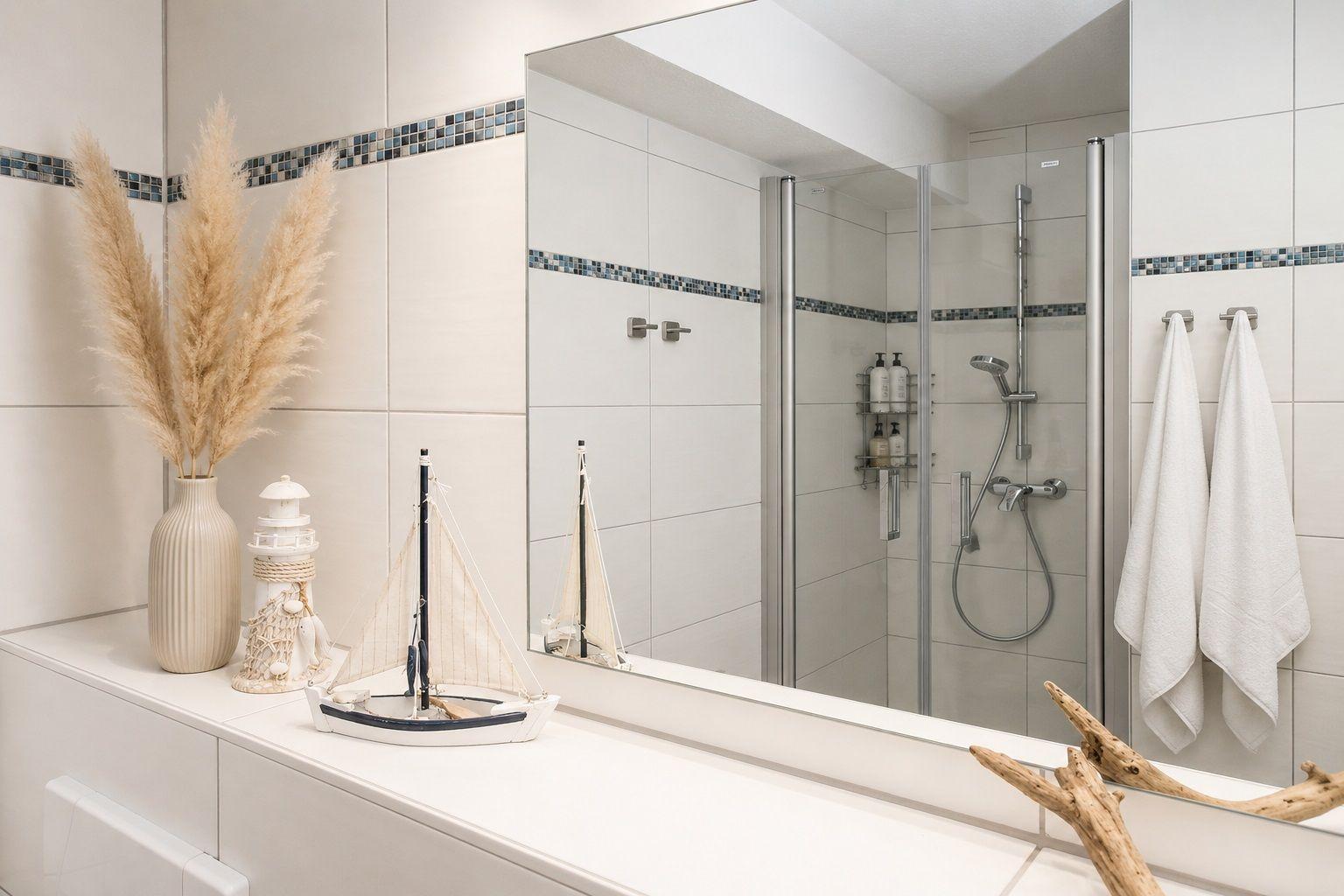 Badezimmer mit Spiegel, Dusche und Dekoration. Weiße Fliesen und Handtücher.