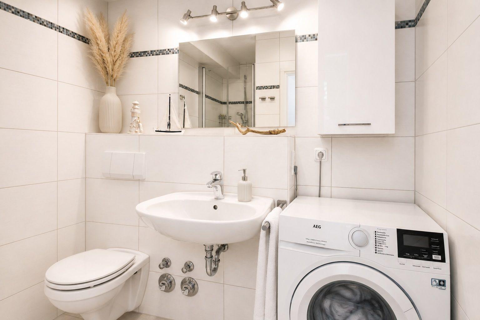 Badezimmer mit Waschmaschine, Spiegel und Toilette. Weiße Fliesen und Dekoration.