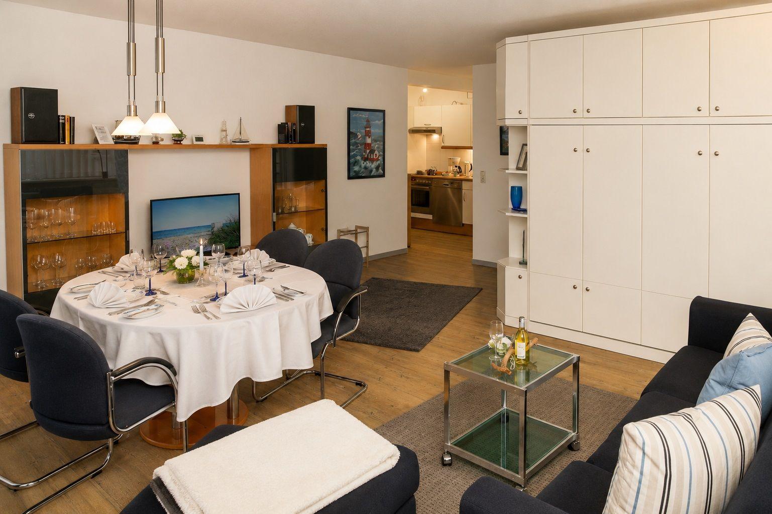 Esszimmer mit gedecktem Tisch, Wohnbereich mit Sofa und Küchenbereich im Hintergrund.