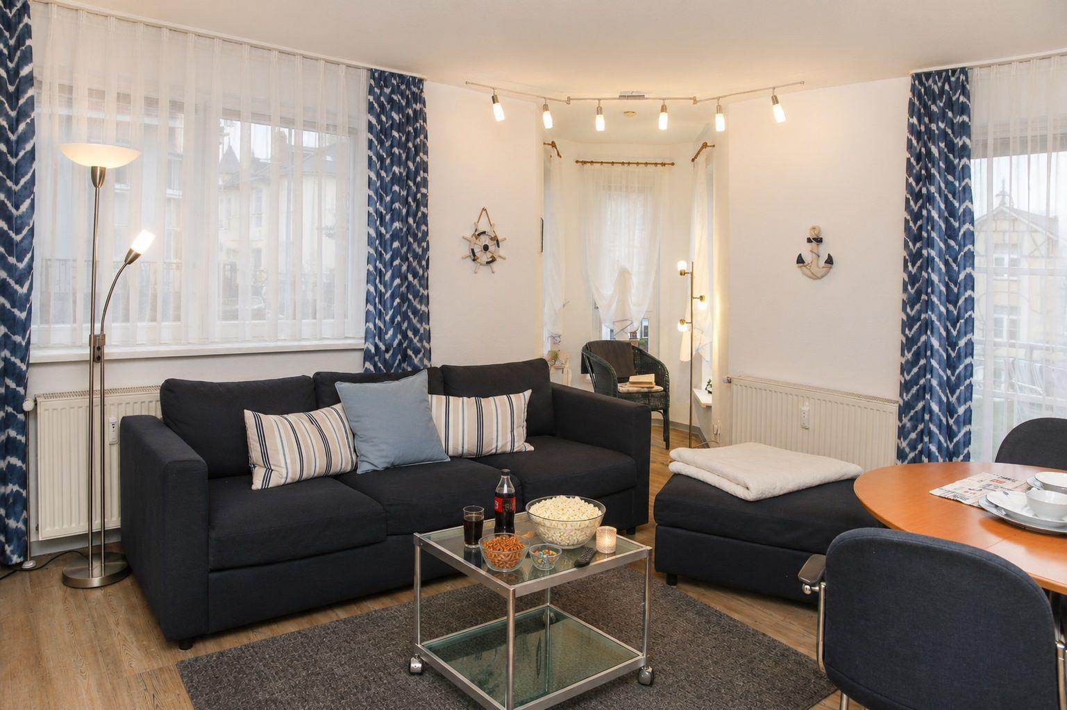 Wohnzimmer mit Sofa, Couchtisch und Essbereich. Blaue Vorhänge und Navigationsdekoration.