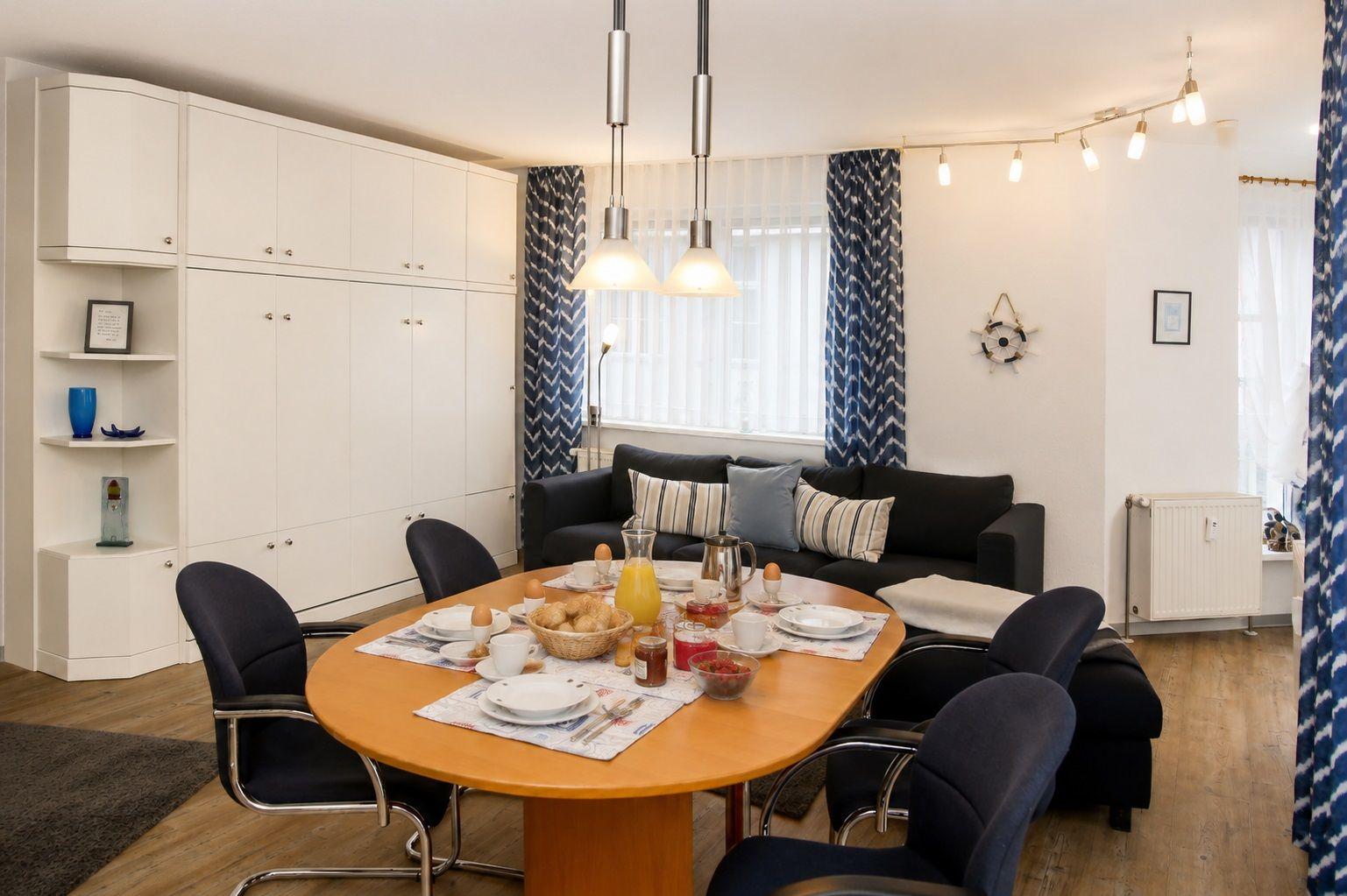 Essbereich mit runder Tisch, schwarzen Stühlen und Sofa. Weiße Schränke und blaue Vorhänge.