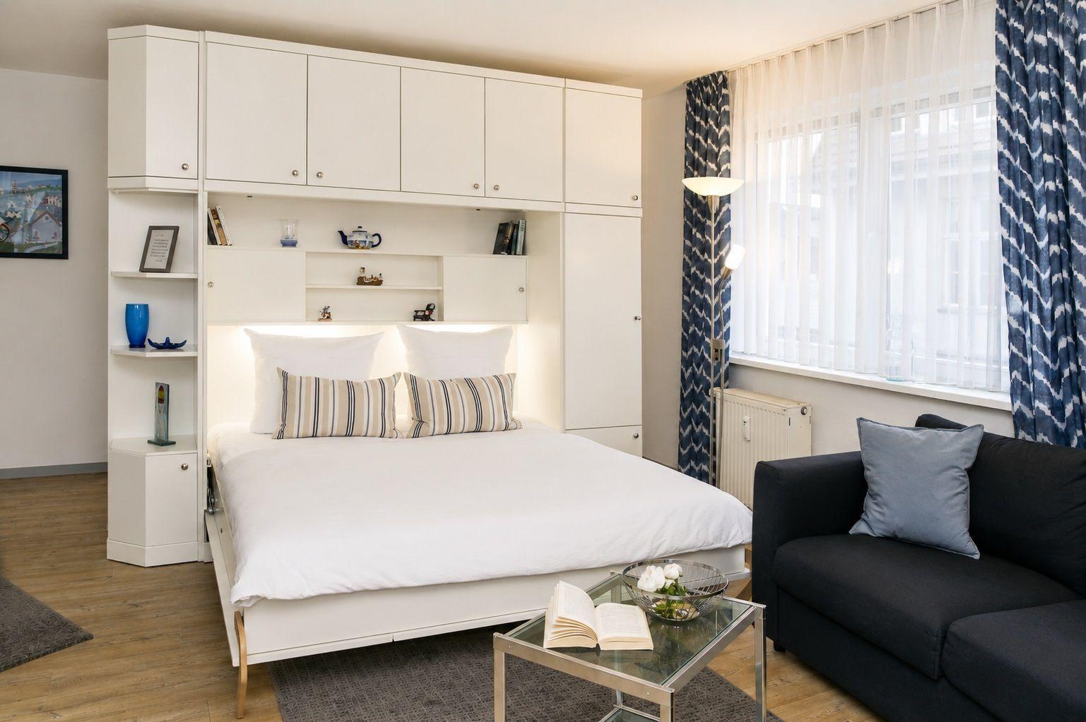 Schlafzimmer mit Bett unter Schrank, Sofa und Glas-Tisch.
