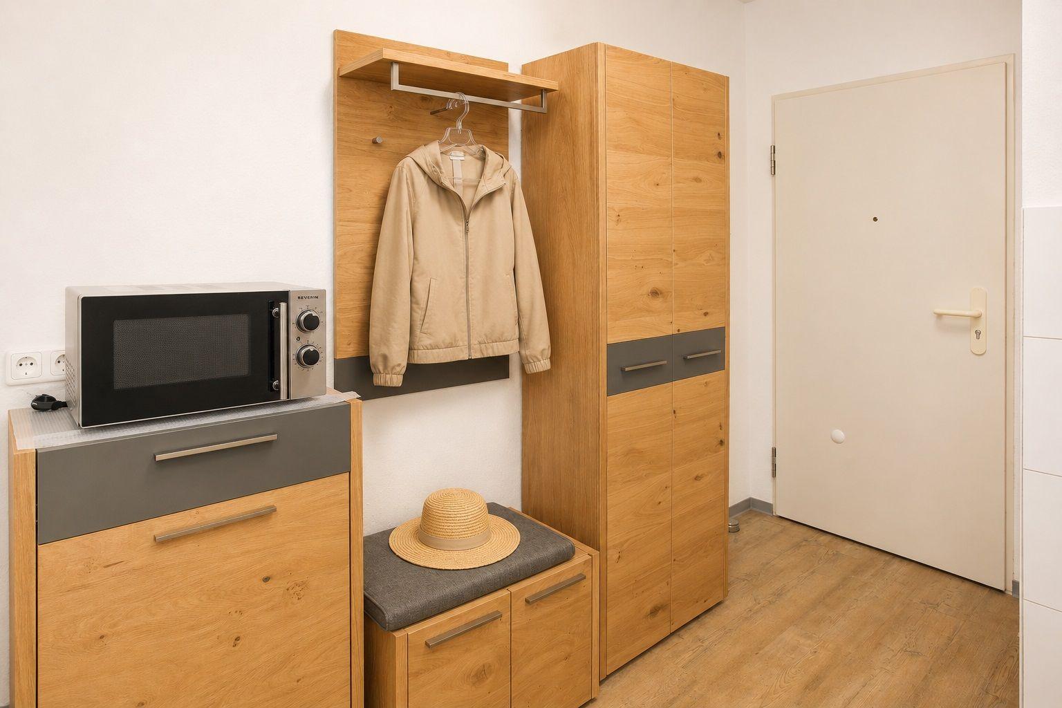 Ein Raum mit Holzmöbeln, Mikrowelle, Kleiderständer und Tür.