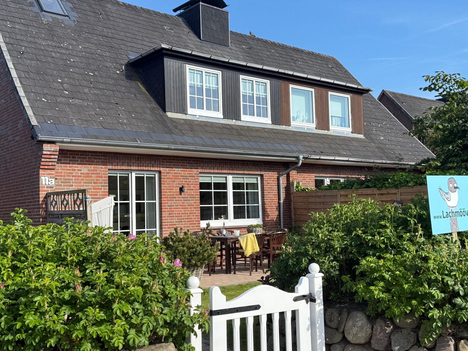 Haus mit Terrasse und Garten. Weiße Türen und Fenster. Schwarze Dachziegel.