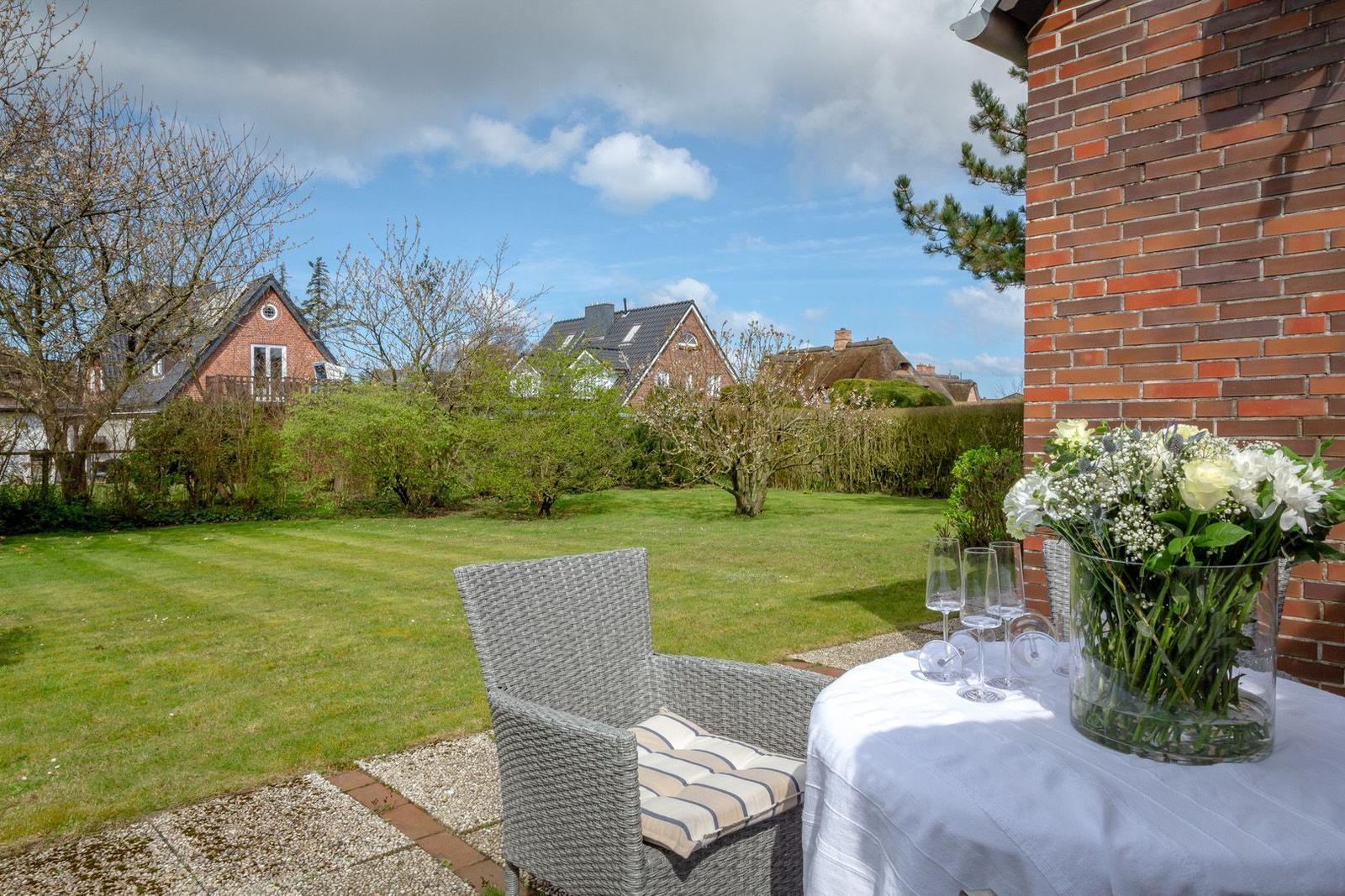 Terrasse mit Tisch, Stühlen und Blumenarrangement. Blick auf grünen Garten und Nachbarhäuser.