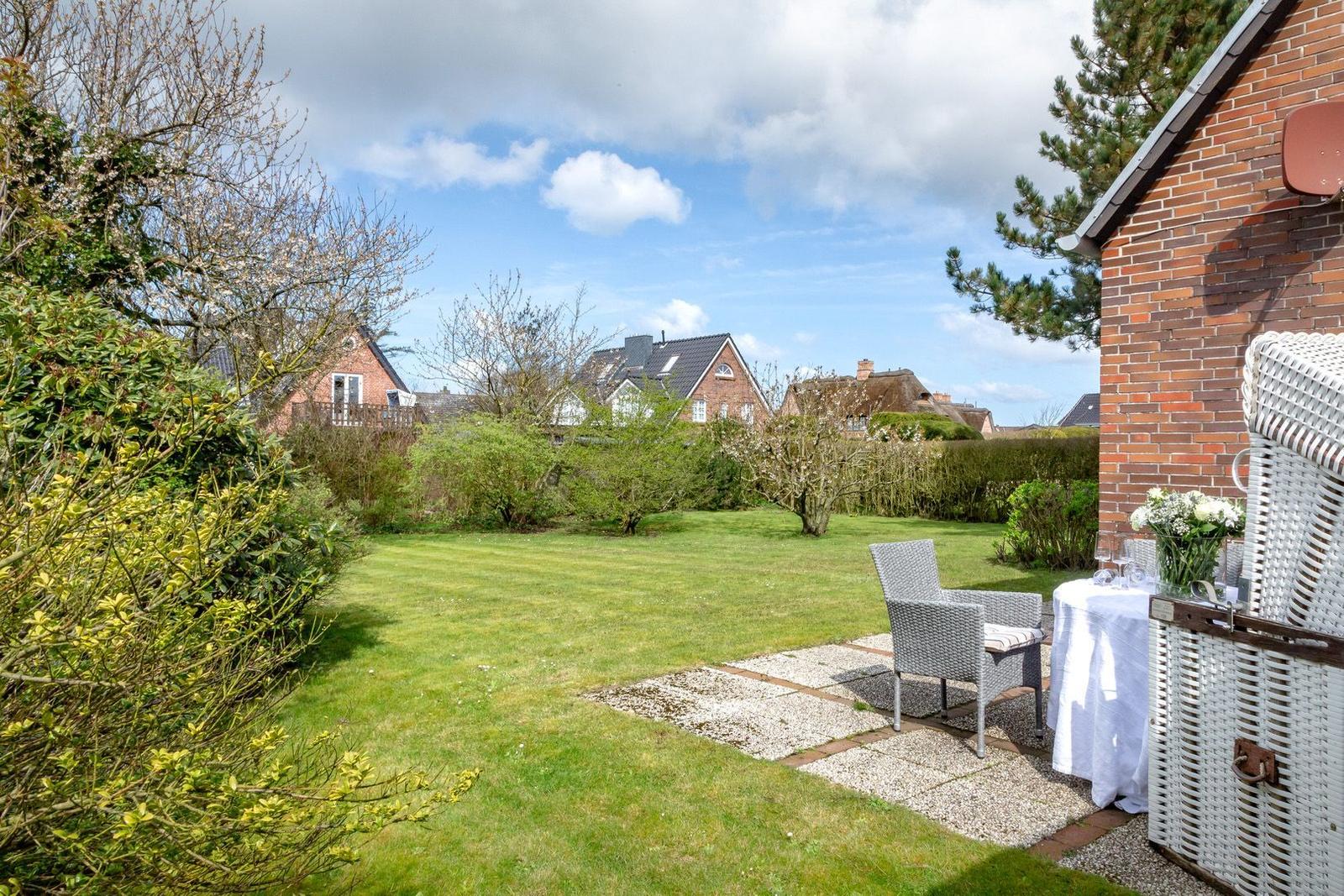 Garten mit Rasenfläche, Tisch und Stühle. Im Hintergrund sind Häuser und Bäume sichtbar.