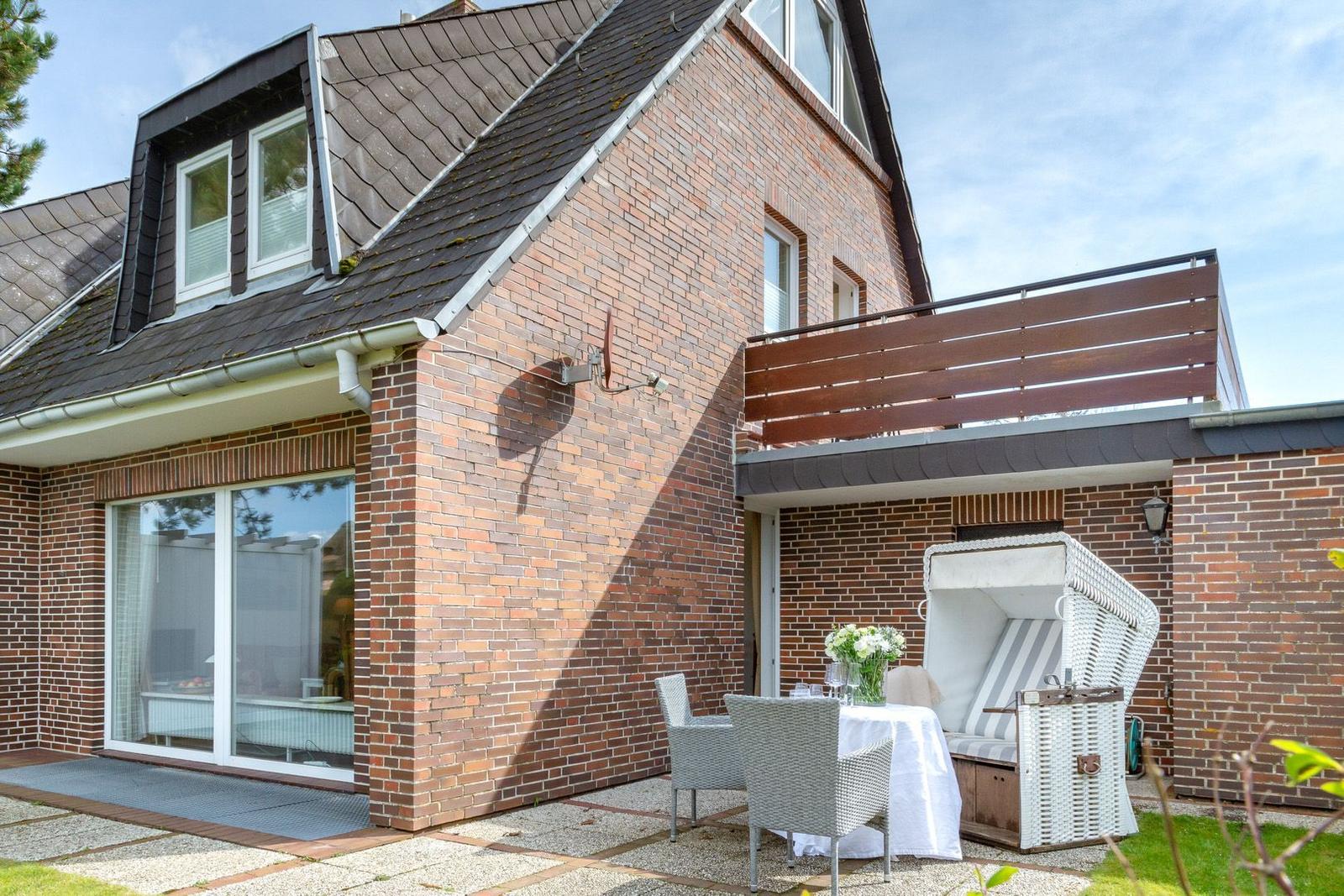 Haus mit Terrasse, Gartenmöbeln und Strandkorb. Zwei Fenster im Dachgeschoss.
