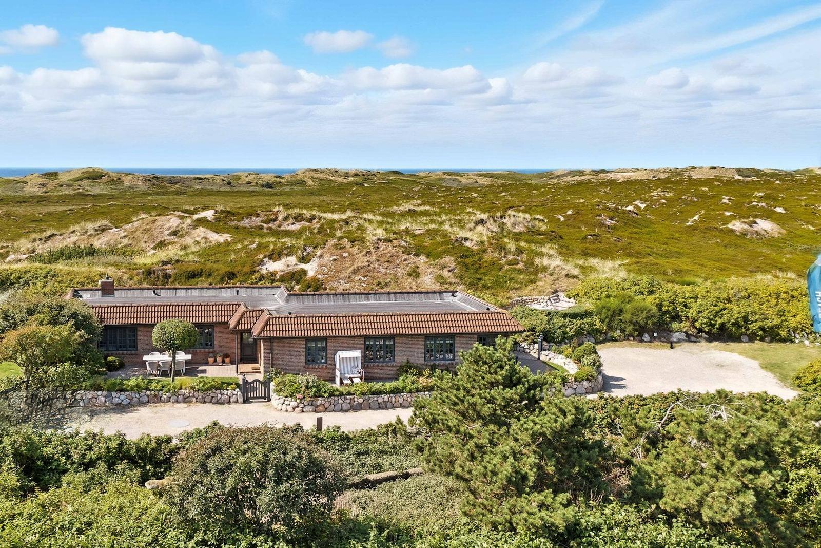 House with terrace and garden, surrounded by dunes and sea.