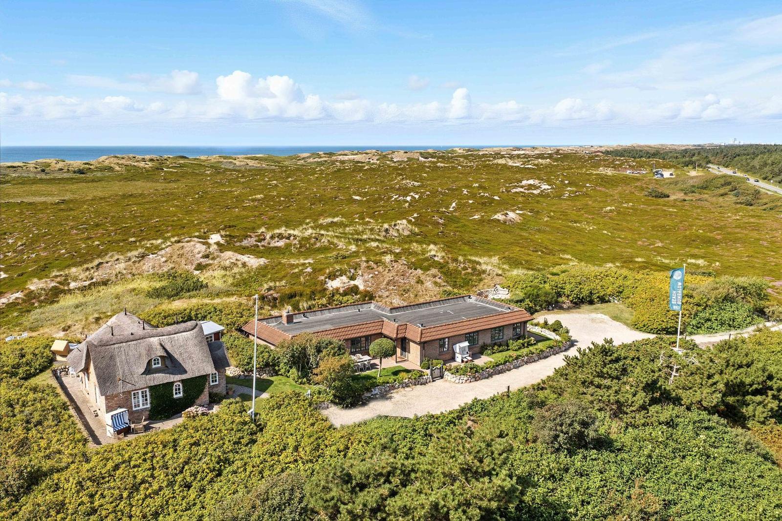 Haus mit Dach aus Stroh und moderner Terrasse in grüner Landschaft mit Blick aufs Meer.