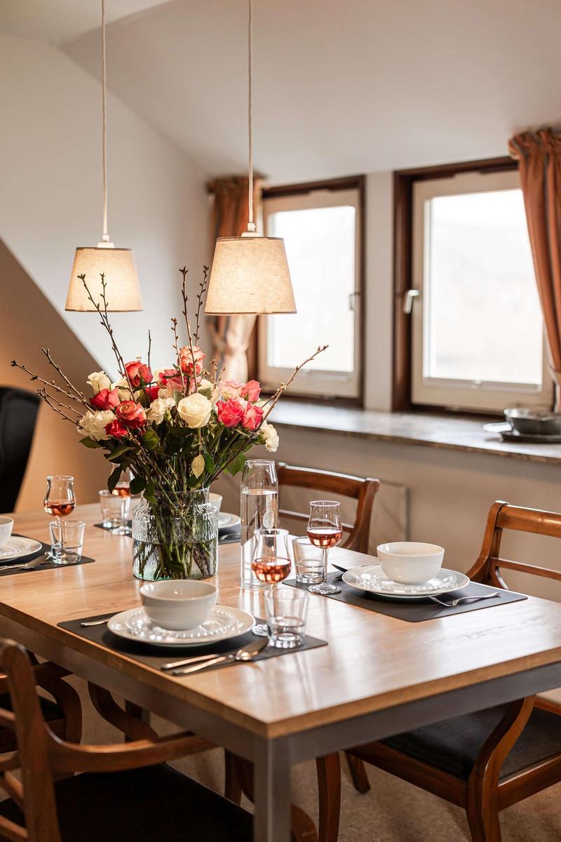 Esstisch mit Blumenarrangement und Gläsern vor Fenstern mit Holzrahmen.