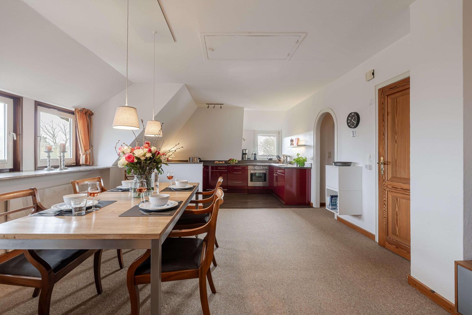 Essbereich mit Tisch und Stühlen, Küche mit roten Schränken und Fenster.