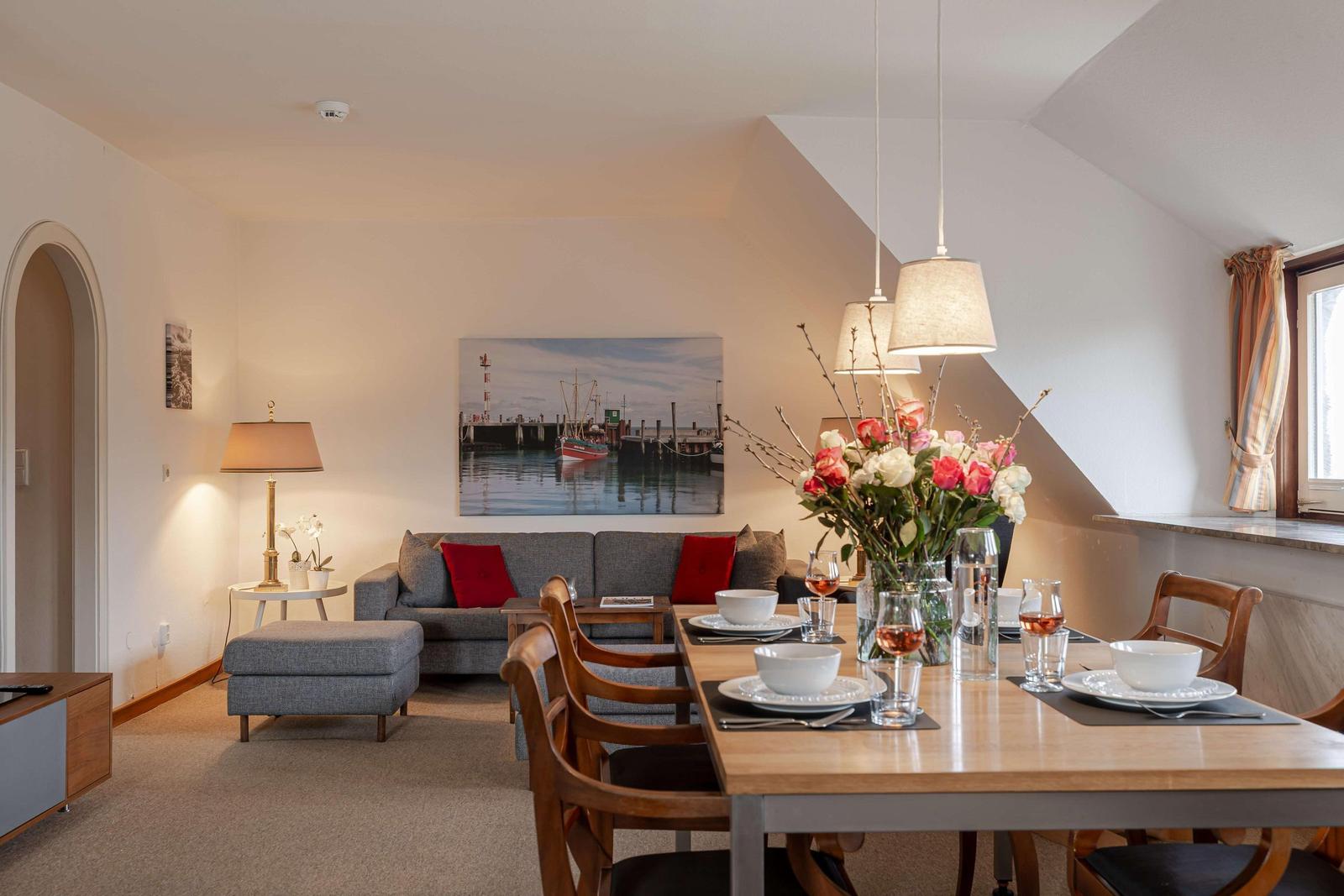 Esszimmer mit Tisch, Stühlen und Blumen. Wohnbereich mit Sofa und Wandbild.