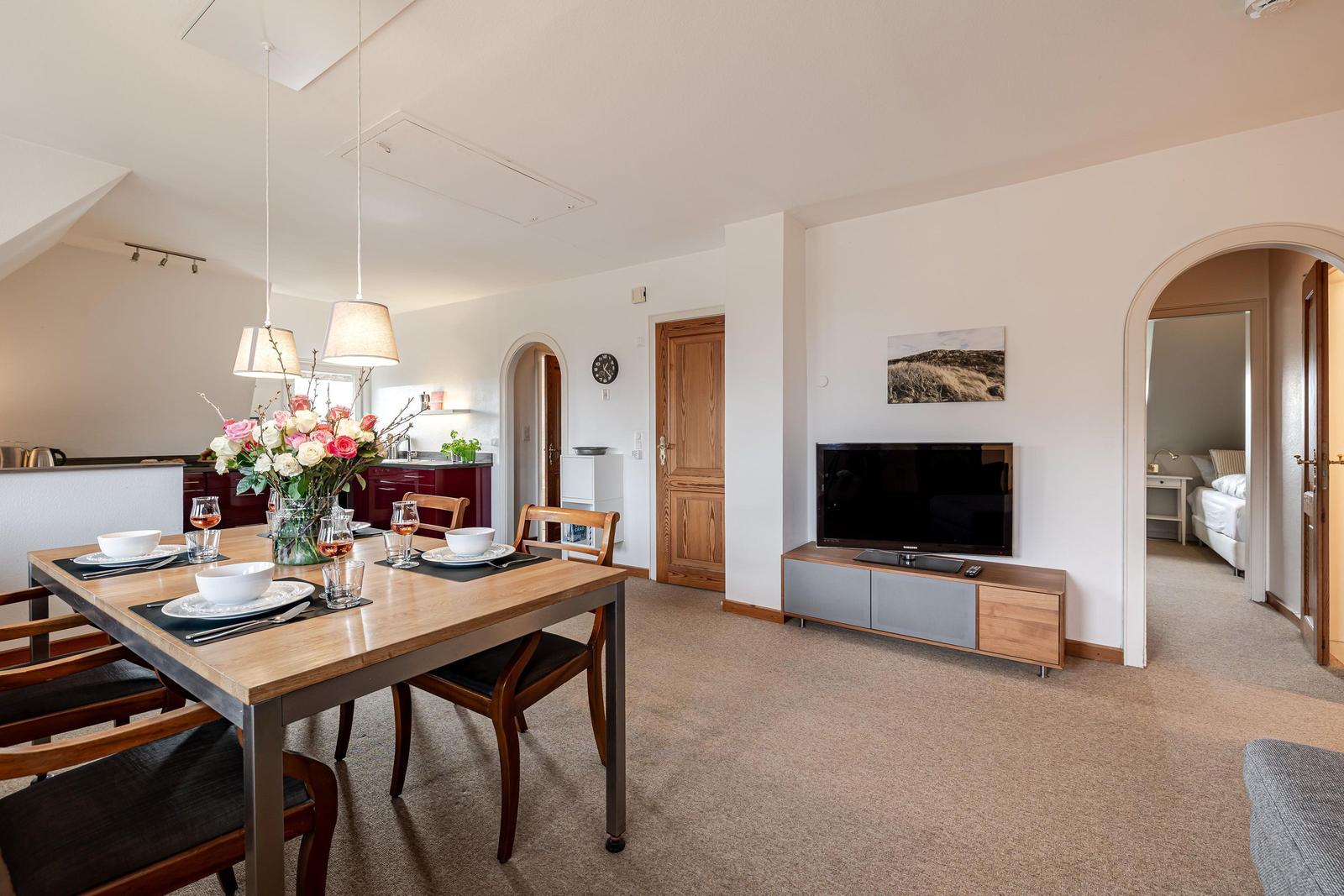 Essbereich mit Tisch und Stühlen, Wohnzimmer mit Fernseher und Schlafzimmer im Hintergrund.