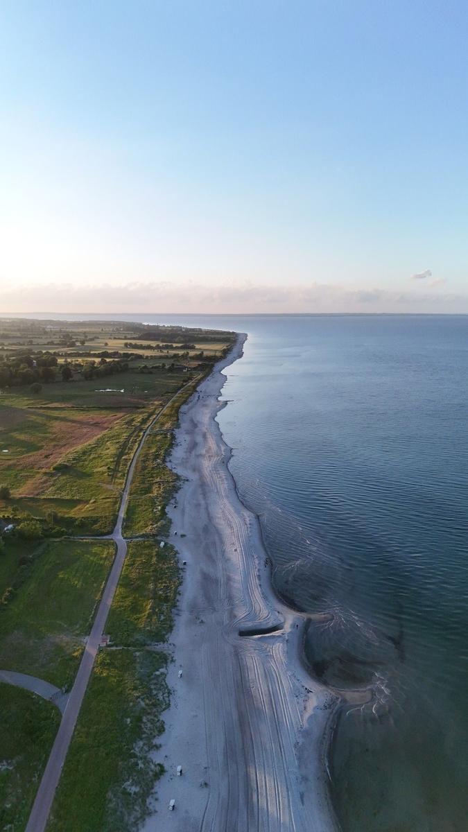 Aerielansicht einer Küstenlinie mit Strand, Grünflächen und ruhigem Wasser.