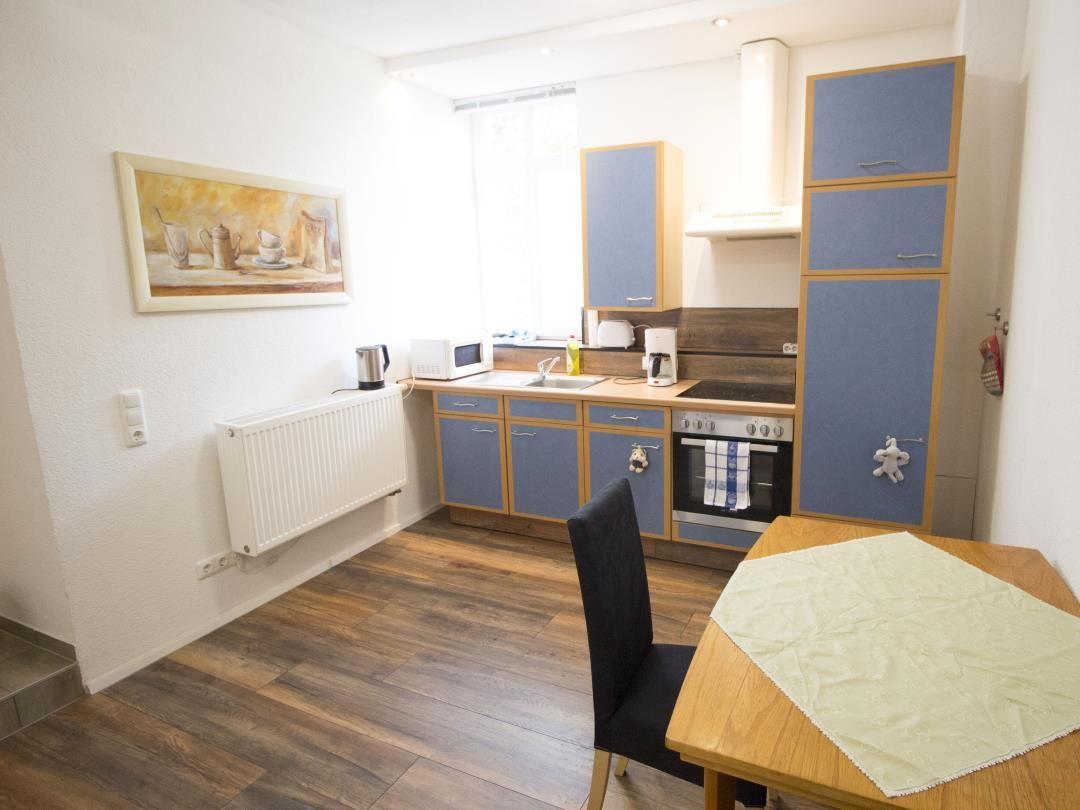 Küche mit blauen Schränken, Tisch und Stuhl. Wandbild und Heizung sind sichtbar.