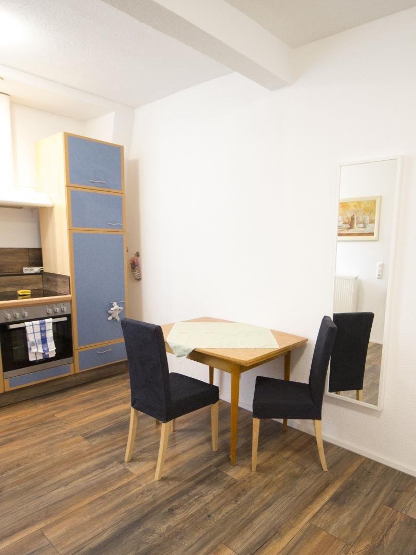 Essbereich mit Tisch und zwei Stühlen neben Küchenzeile mit Ofen und Hochschrank.