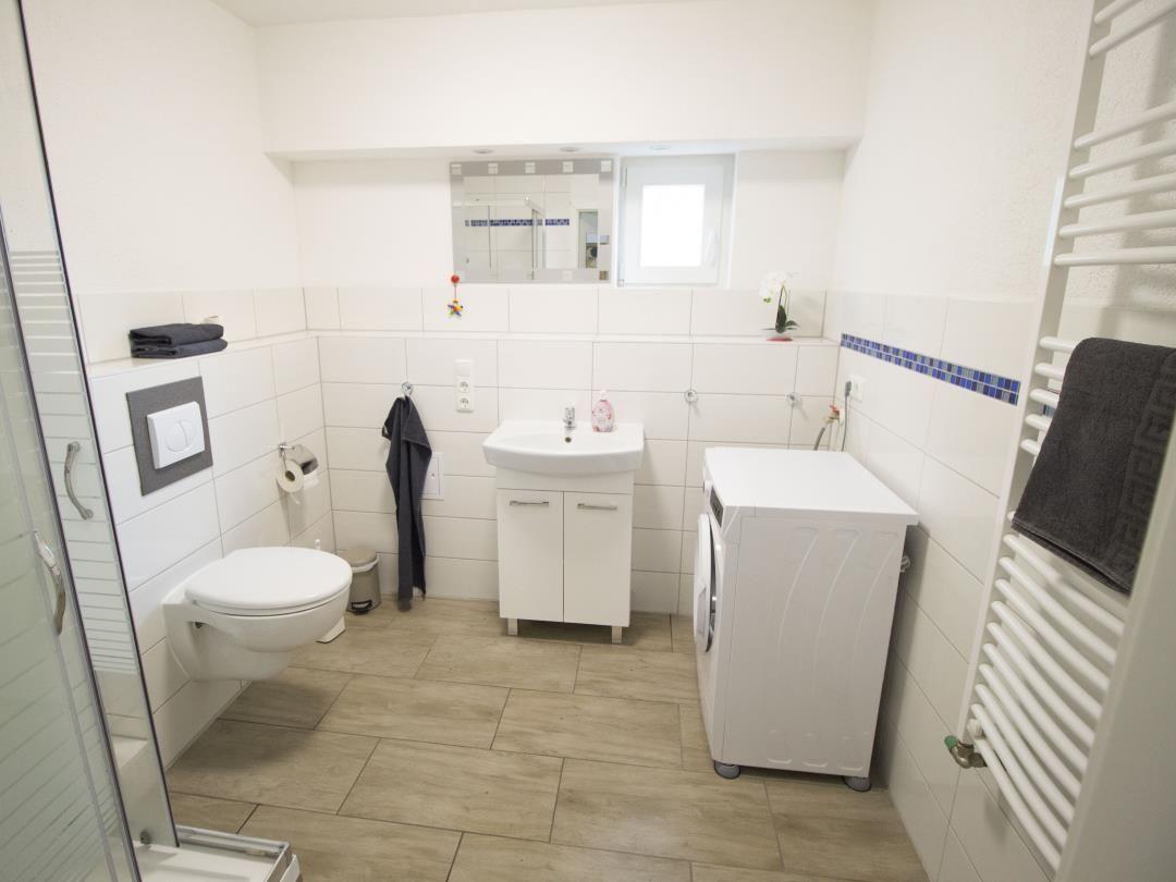 Badezimmer mit Dusche, Toilette, Waschbecken und Waschmaschine.