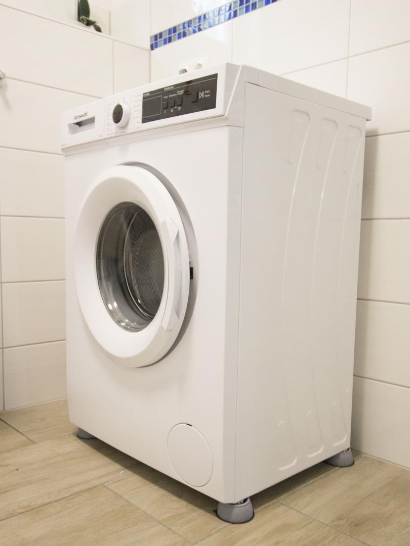 Eine weiße Frontlader-Waschmaschine in einem hellen Raum mit Fliesenwand.