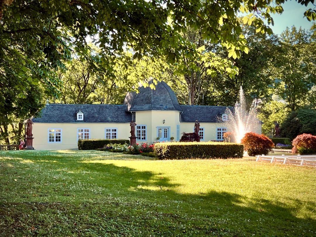 Haus mit Garten, Brunnen und Statuen unter Bäumen.