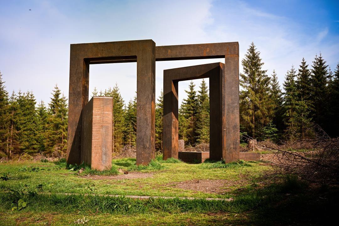 Große Metallskulptur mit mehreren Öffnungen in einem Waldgebiet.