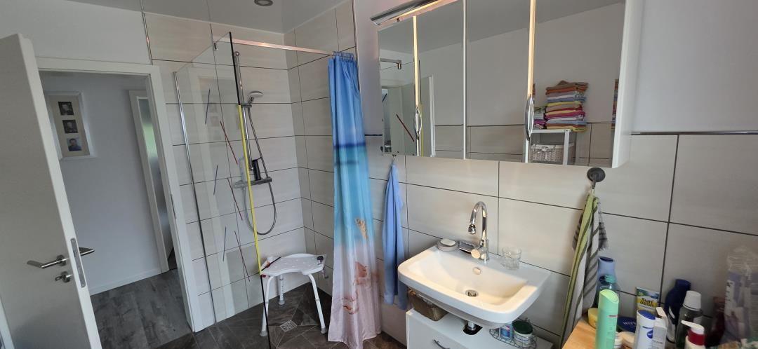 Badezimmer mit Dusche, Waschbecken und Spiegelschrank. Duschvorhang und Handtuch hängen.