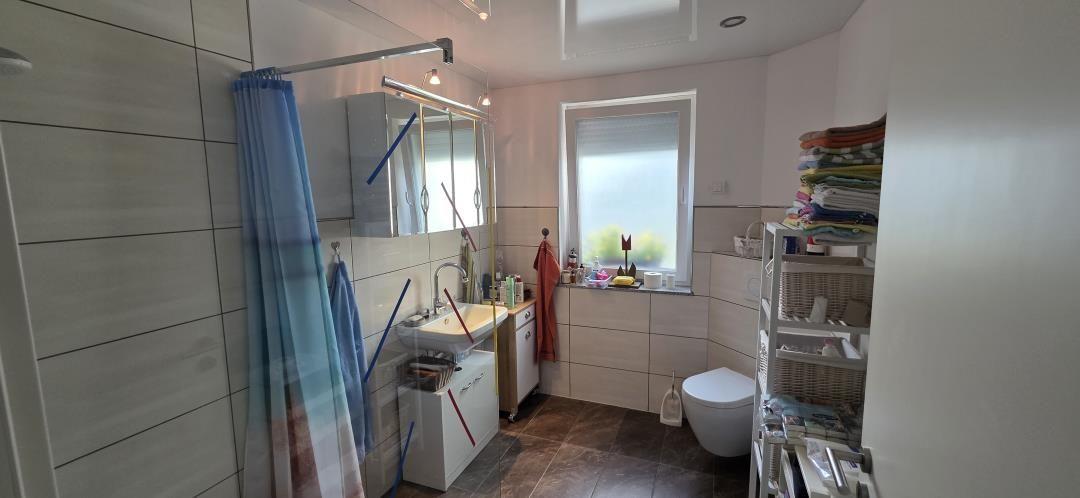 Badezimmer mit Dusche, Waschbecken und Toilette. Fenster mit Jalousie und Handtücher auf Regal.