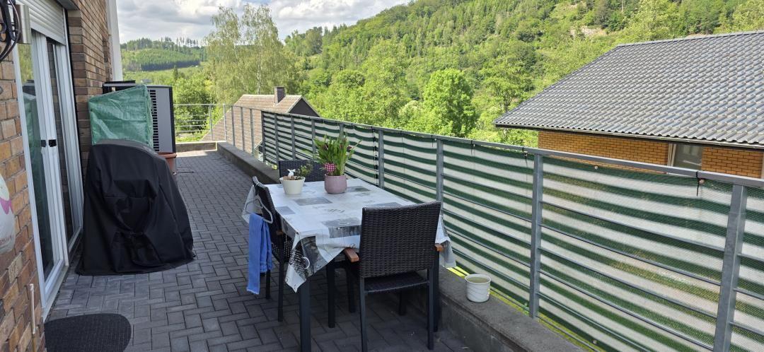 Terrasse mit Tisch, Stühlen und Blick auf grüne Hügel.