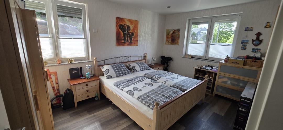 Schlafzimmer mit Doppelbett, zwei Fenstern und Holzmöbeln.