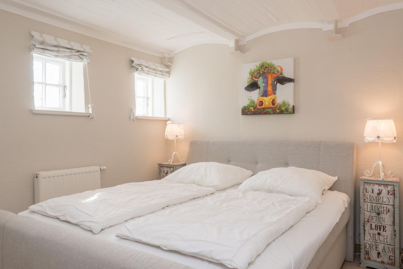 Schlafzimmer mit Bett, zwei Nachttischen und Wandbild einer Kuh.