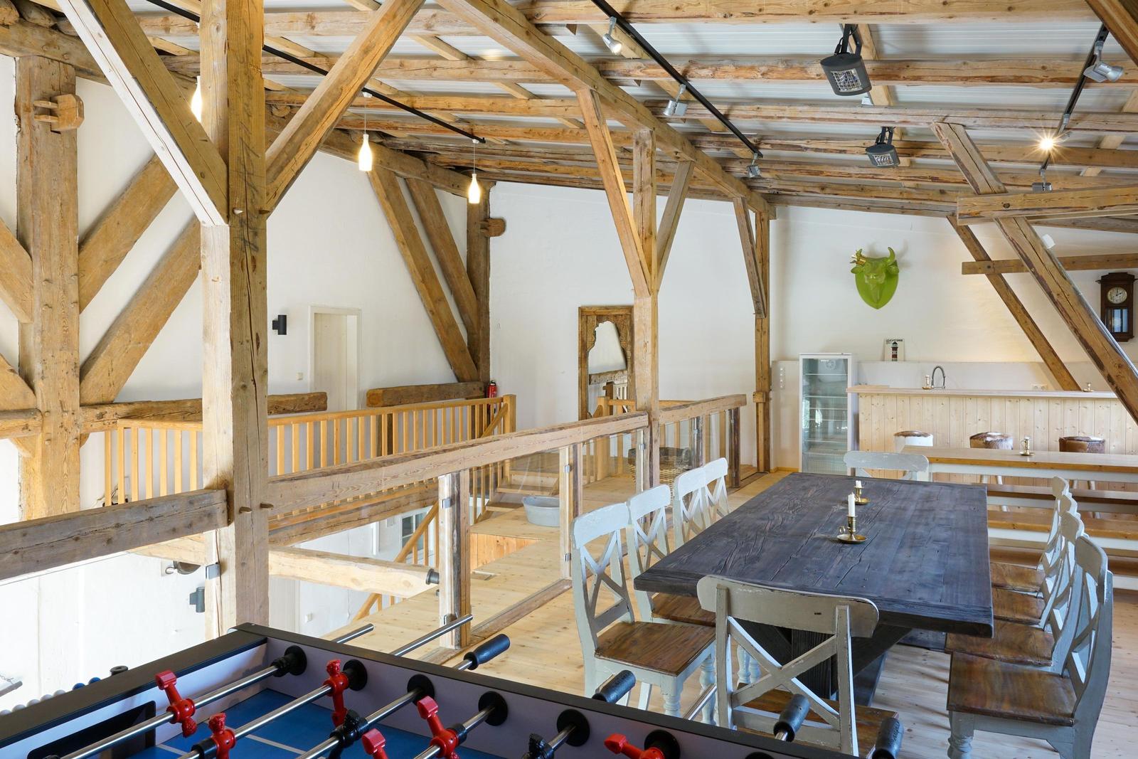 Großer Raum mit Holzkonstruktion, Esstisch, Küchenbereich und Tischfußball.