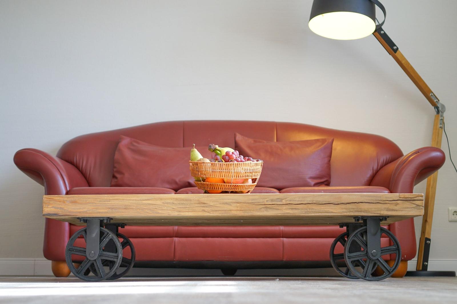 Roter Ledersofa mit Korb voller Früchte und industrieller Couchtisch mit Rädern.