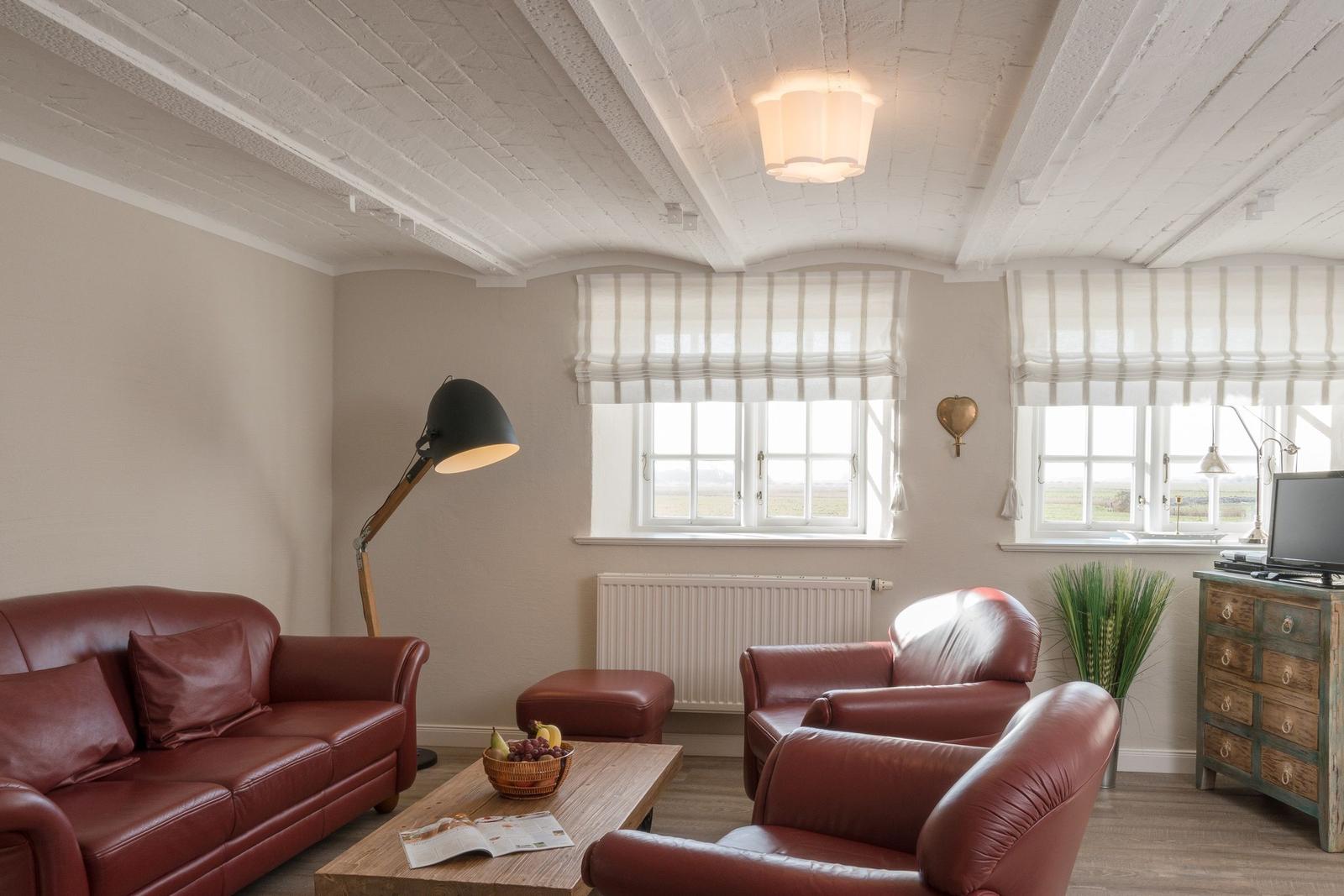 Wohnzimmer mit rotem Ledersofa, zwei Sesseln und Holztisch unter weißem Deckenbalken.