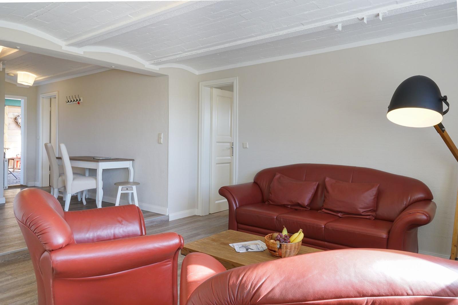 Wohnzimmer mit rotem Ledersofa, zwei Sesseln und Holztisch. Hintergrund zeigt Essbereich.