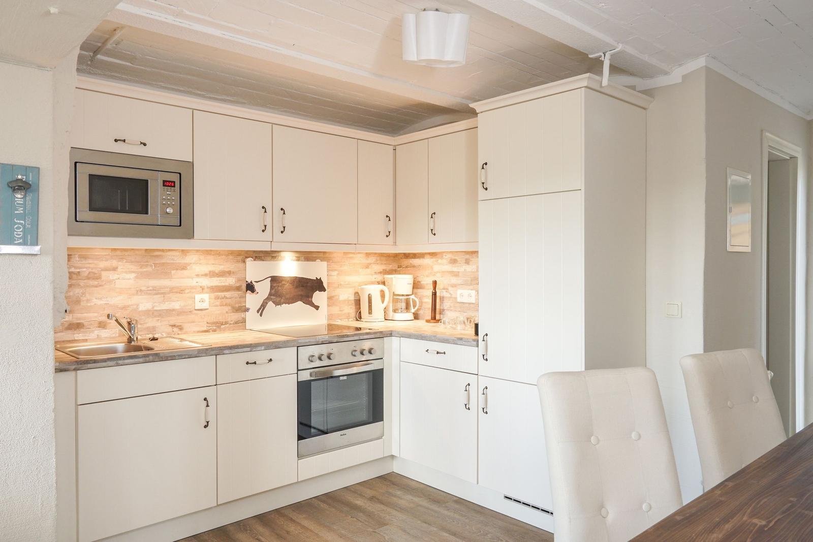 Küche mit weißen Schränken, Edelstahlgeräten und Holzoptik an der Wand.