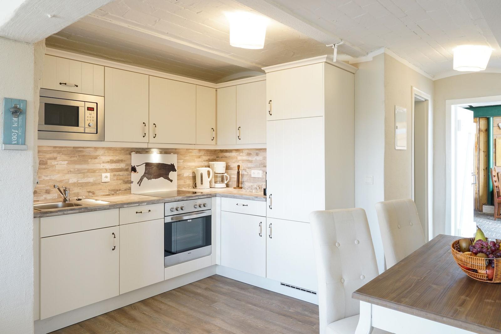 Küche mit weißen Schränken, Edelstahlgeräten und Holzoptik an der Wand.